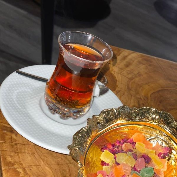 Turks theeglas op een schoteltje naast een gouden schaaltje met lokum, op een houten tafel in de zaak